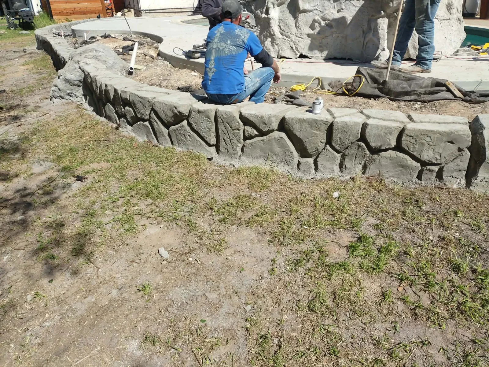 Textured concrete retaining wall with stone-pattern blocks during installation on residential property