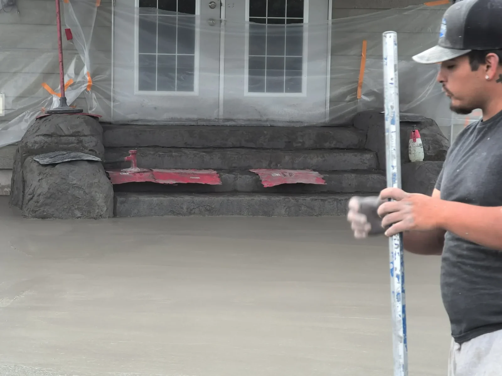 Concrete slab finishing with level tool, protective plastic sheeting, and safety barriers