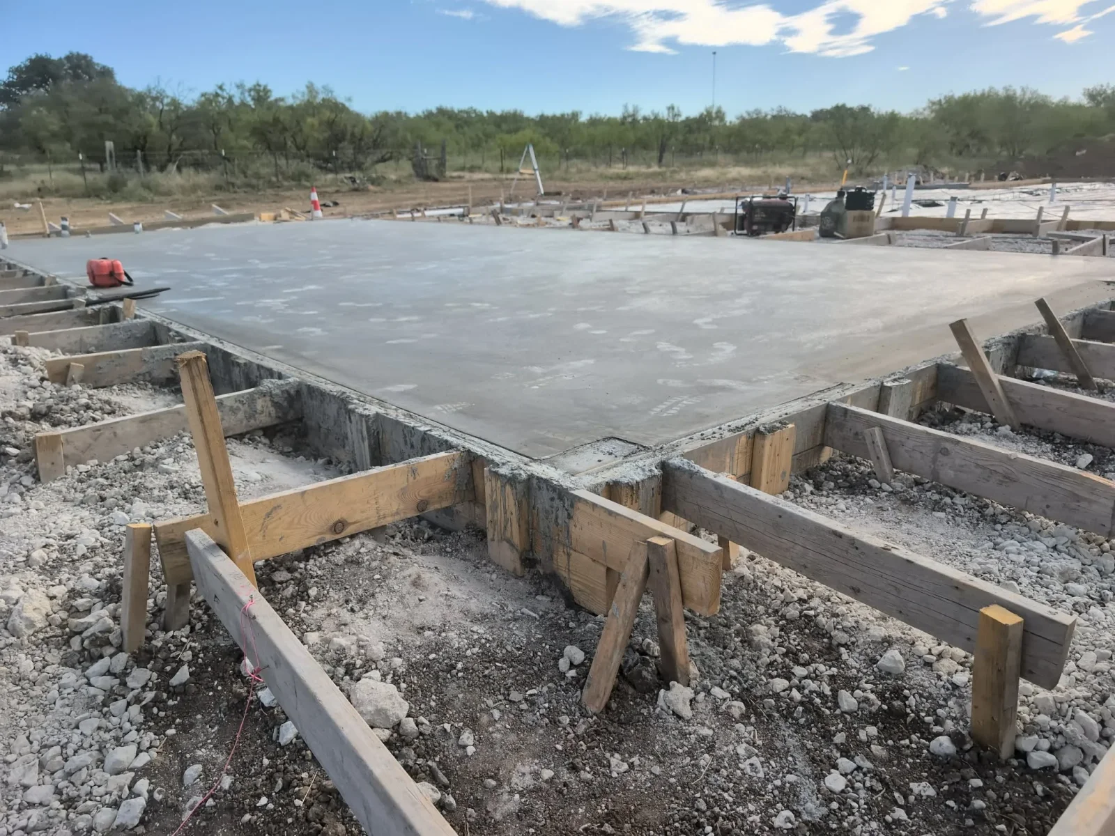 Finished concrete foundation slab with wooden forms, aggregate base, and grade beams on construction site