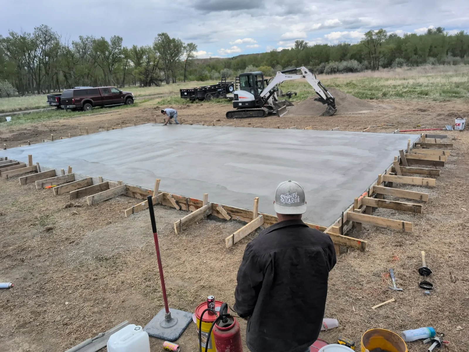 Concrete foundation slab with wooden forms, finished concrete surface, and construction crew on-site