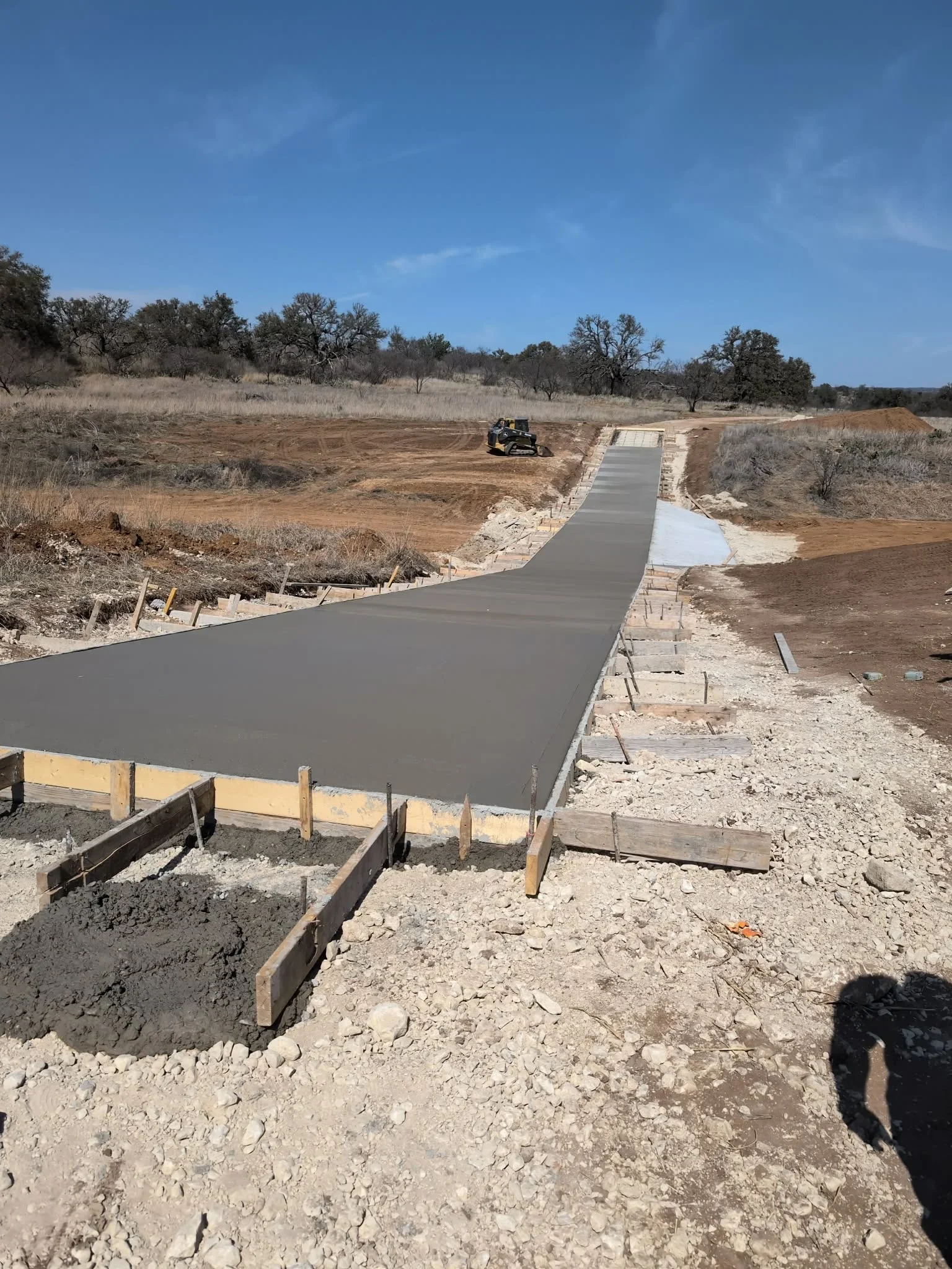 Concrete driveway on sloped terrain with wooden forms and gravel base, erosion control visible