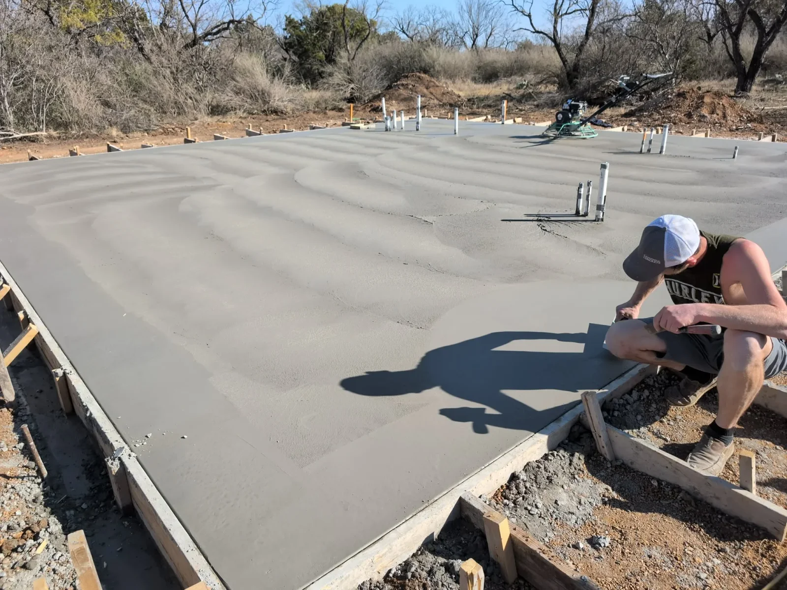 Concrete foundation slab with finished surface, anchor bolts, and post sleeves during curing
