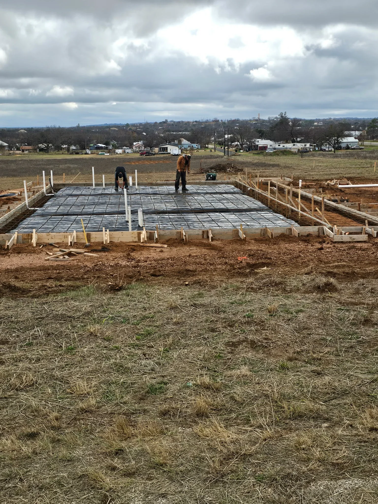 Concrete foundation slab with rebar grid, wooden forms, and support posts during installation