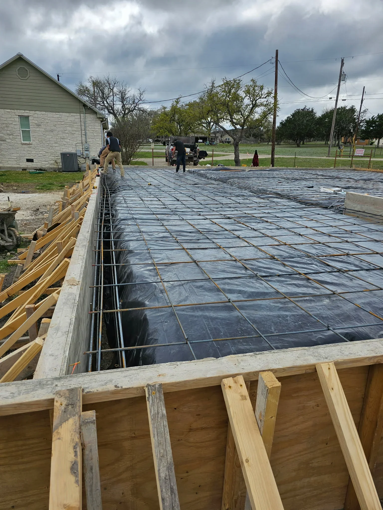 Reinforced concrete foundation with rebar grid, vapor barrier, and wooden forms on residential lot