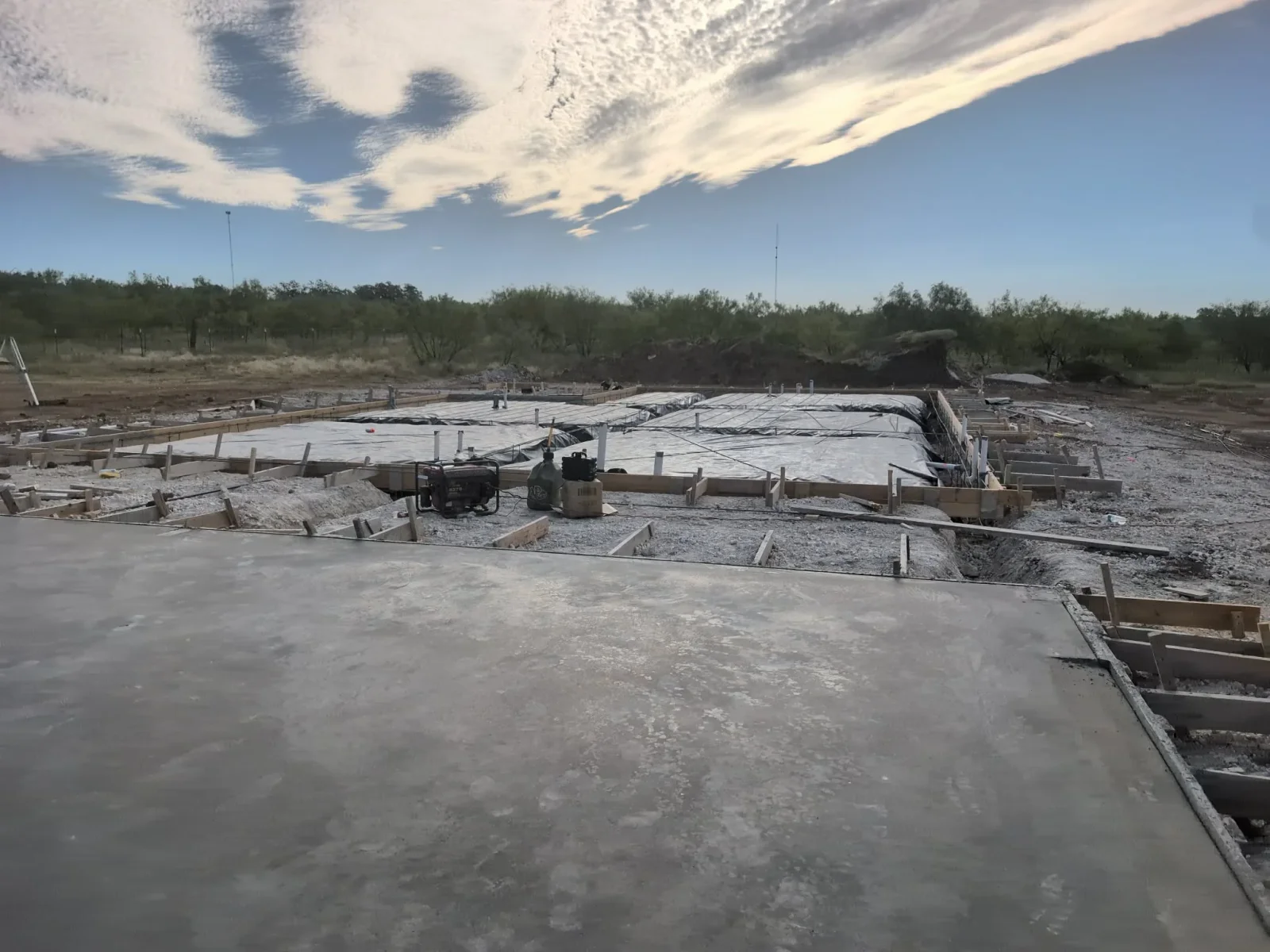 Freshly poured concrete foundation with wooden forms and support posts on desert property