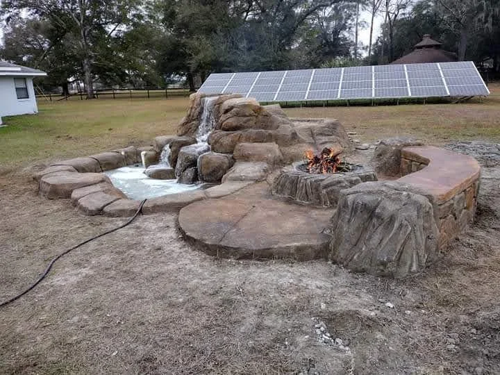 Stacked stone fire pit with concrete seating pads and rustic stone surround in rural setting