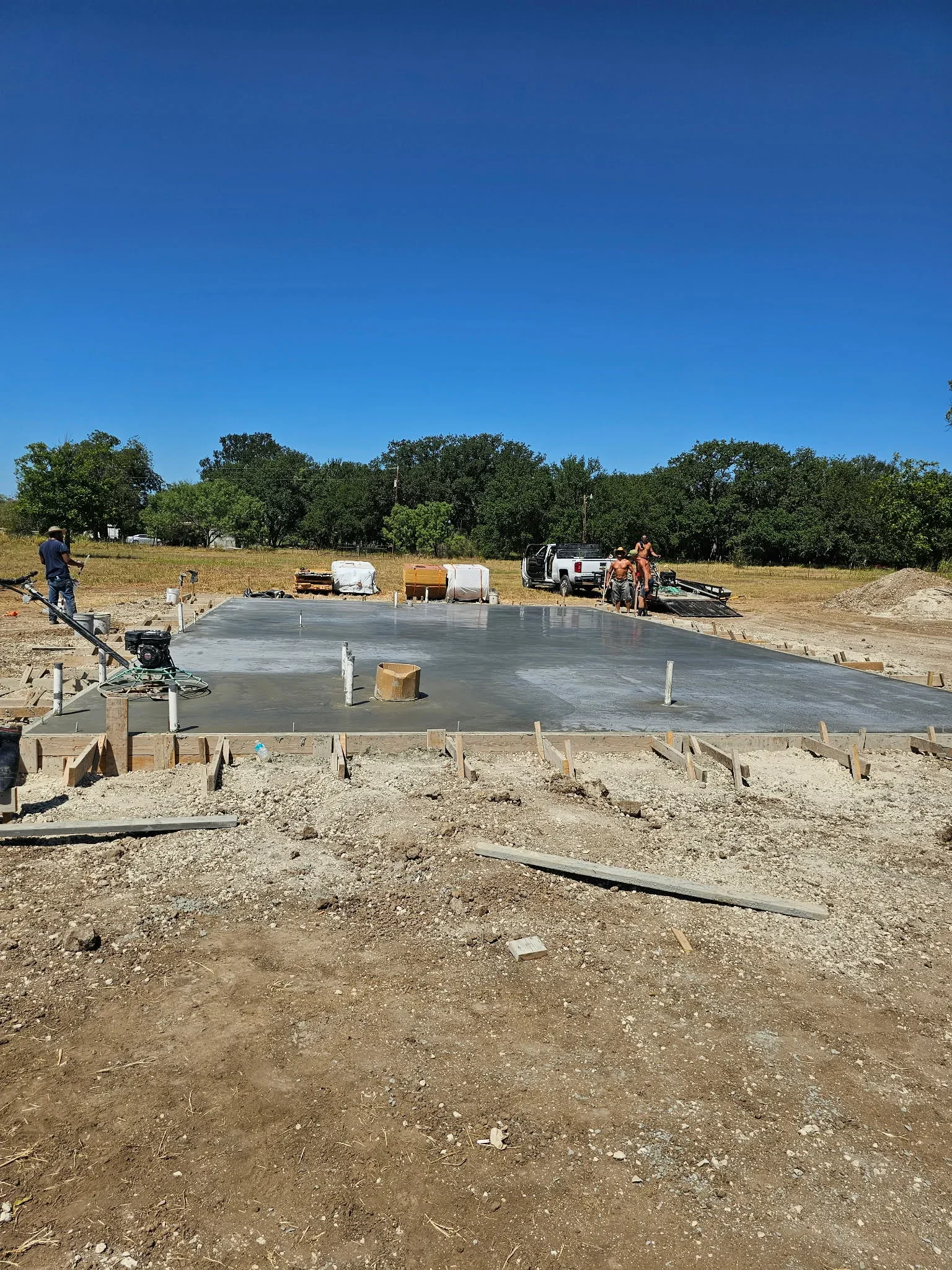 Freshly poured concrete foundation slab with wooden forms and support posts during finishing