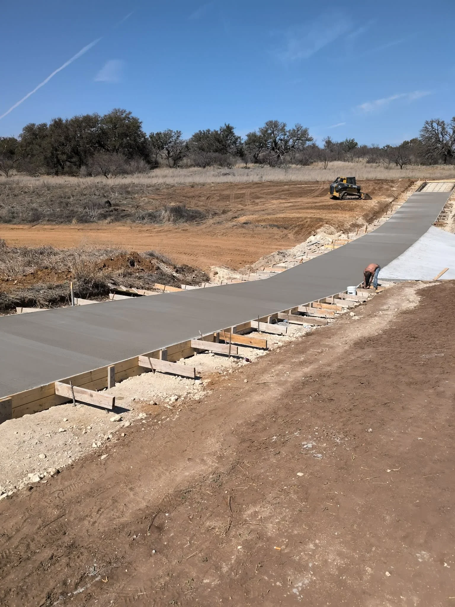 Concrete driveway with wooden forms and gravel base on sloped rural terrain