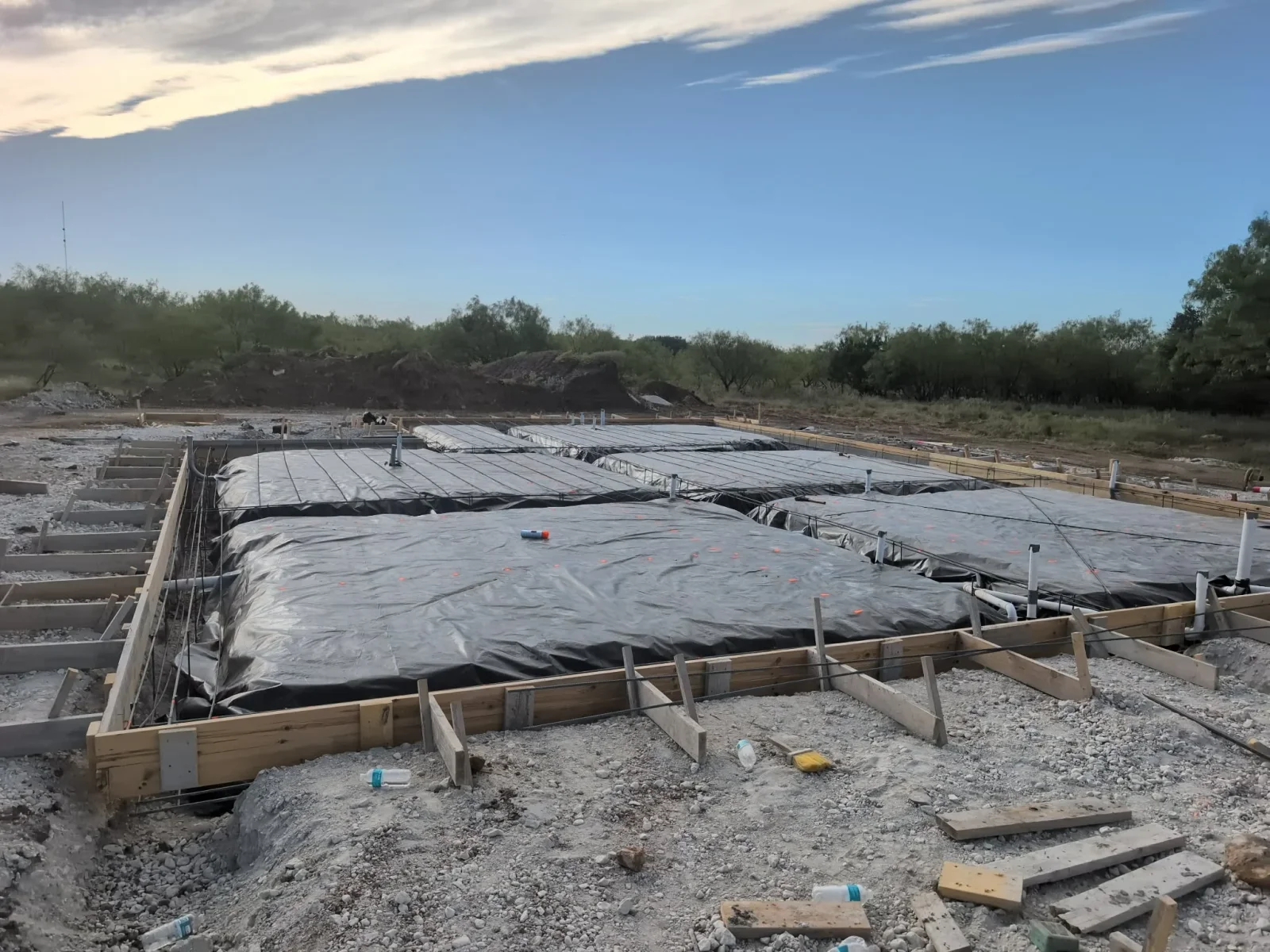 Multiple concrete slabs with plastic protection and wooden forms on prepared gravel base