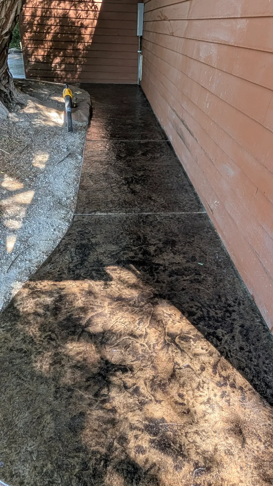 Stamped and stained decorative concrete walkway with dark finish between brick wall and structure