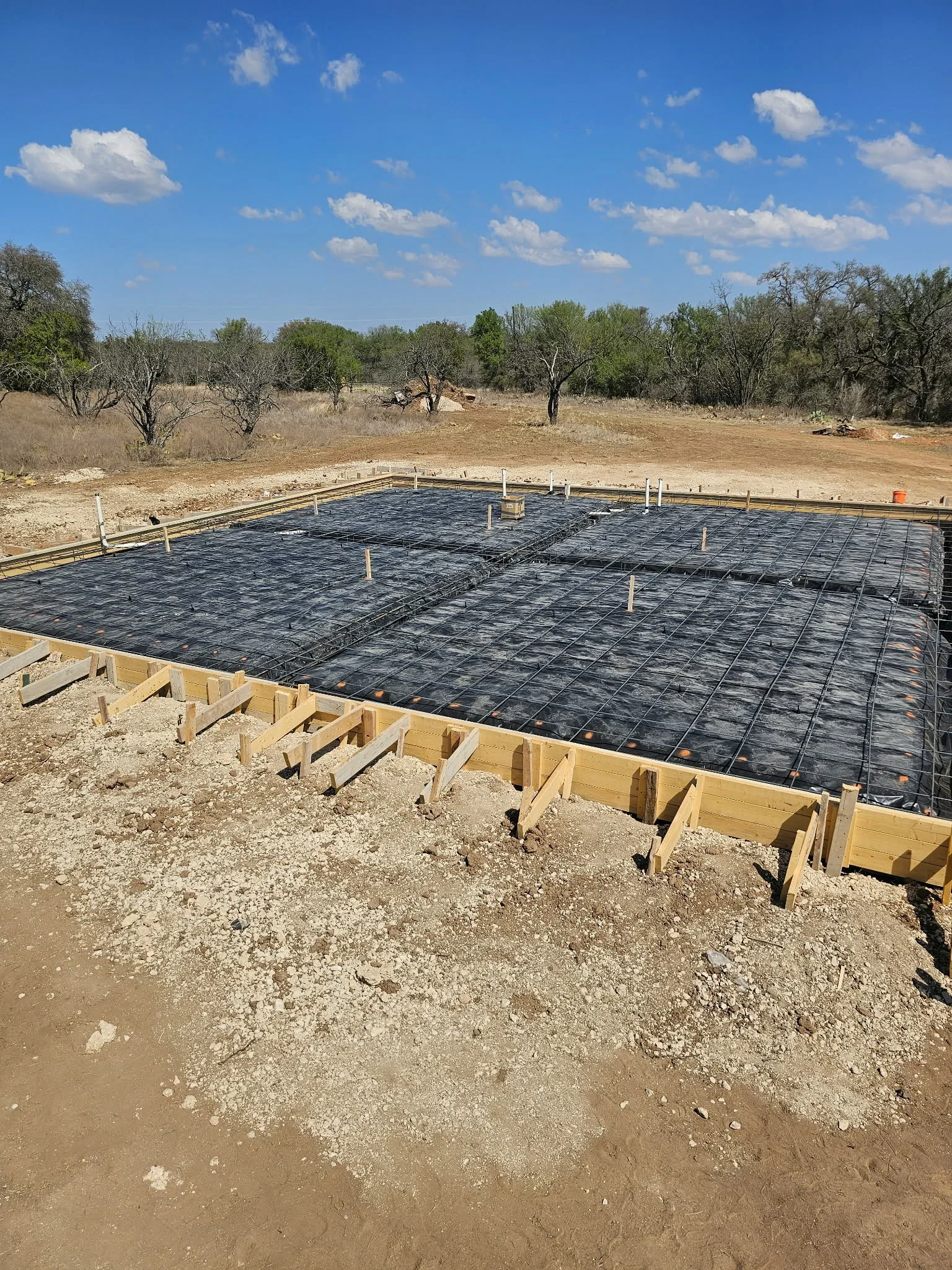 Concrete foundation with rebar grid, wooden forms, and prepared subgrade on rural property