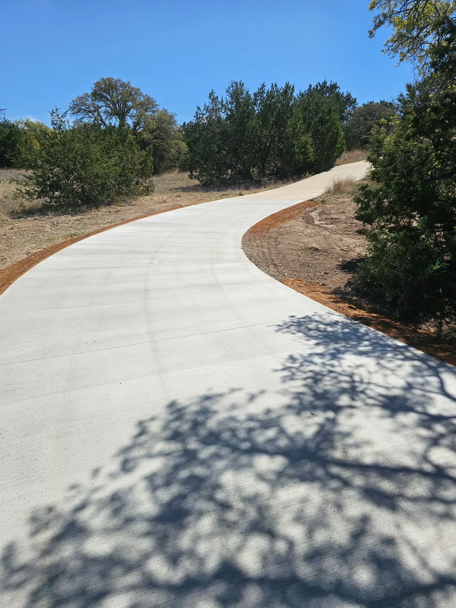 Curved concrete driveway with control joints, mulched borders, and surrounding landscaping on sloped terrain