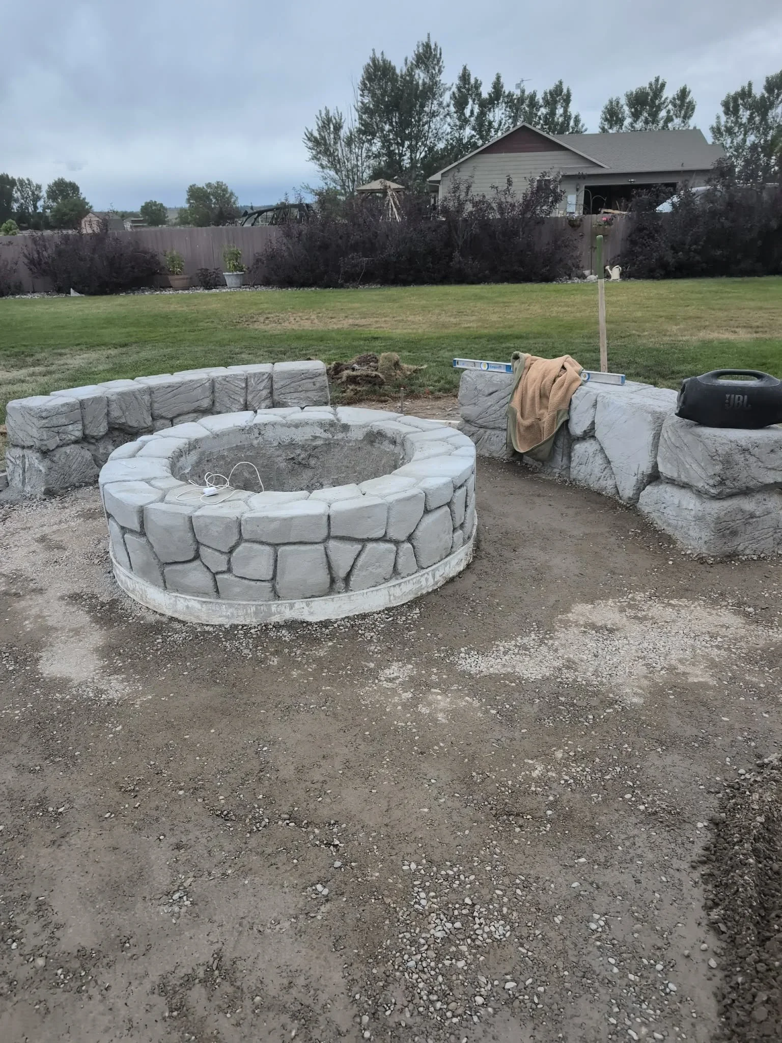 Circular concrete fire pit with stone texture and matching concrete seating walls in backyard setting