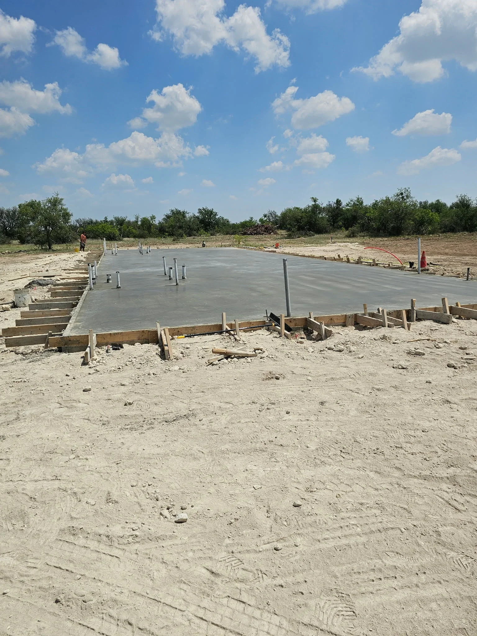 Finished concrete foundation slab with post anchors and wooden forms on prepared ground