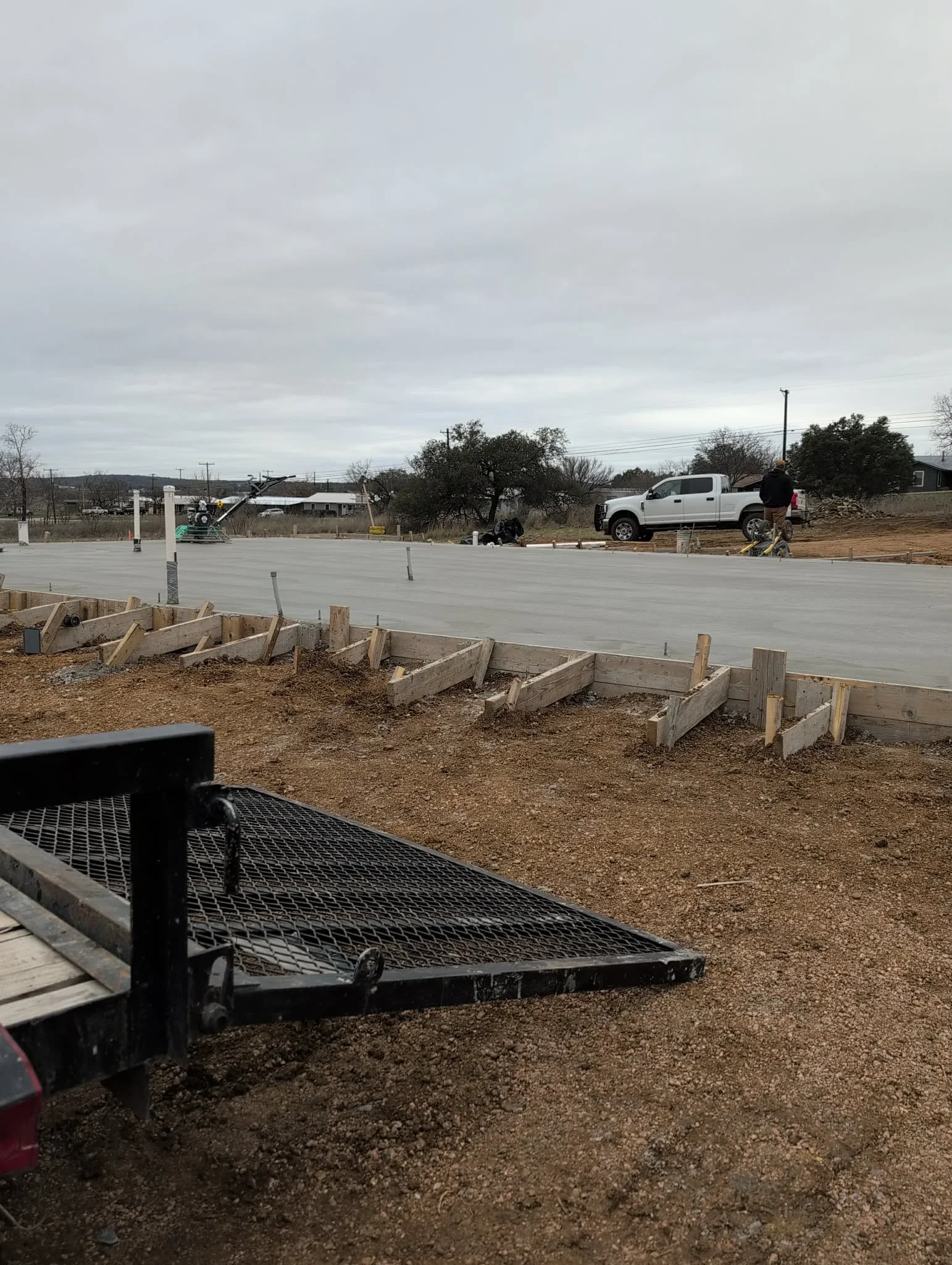 Finished concrete slab with wooden forms, control joints, and support posts on residential foundation